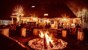 A house with a fire pit in the front yard, surrounded by a wooden fence and trees. - Gite Chalet in the Ardenne, Houffalize. Authentic but Renewed House for 9 People (Houffalize)
