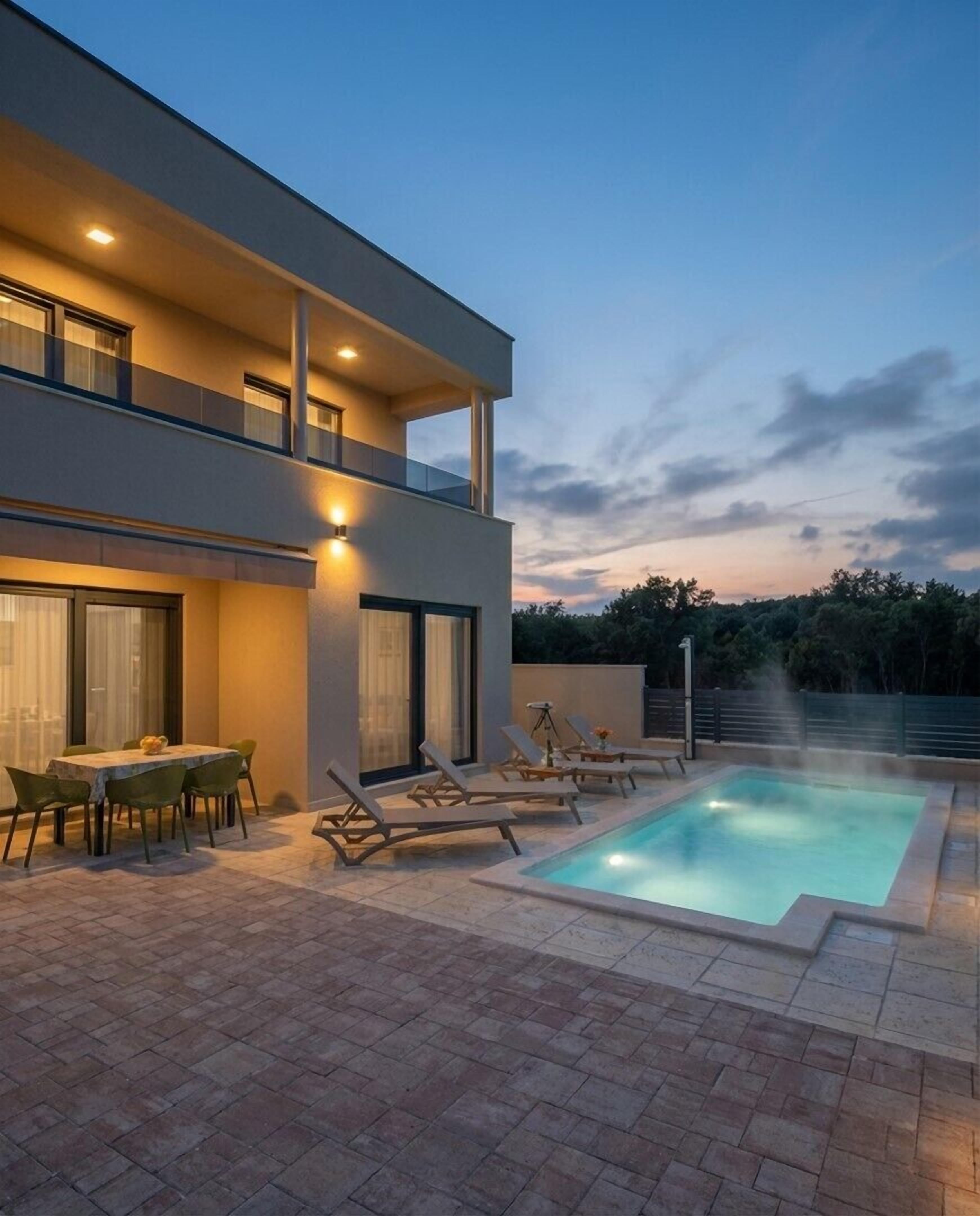 A modern two-story house with a swimming pool, outdoor seating, and a patio area.