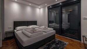 A modern bedroom with a large bed, a dark headboard, and a sliding glass door leading to a balcony.