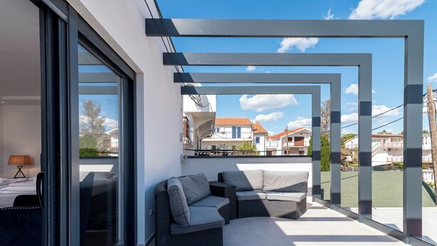 A modern outdoor living area with a sofa and a table, large windows, and a view of the neighborhood.