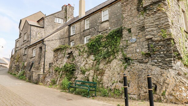 A stone building with a green bench, a cobblestone path, and a clear sky. - 10 Westgate Hill (Pembroke)