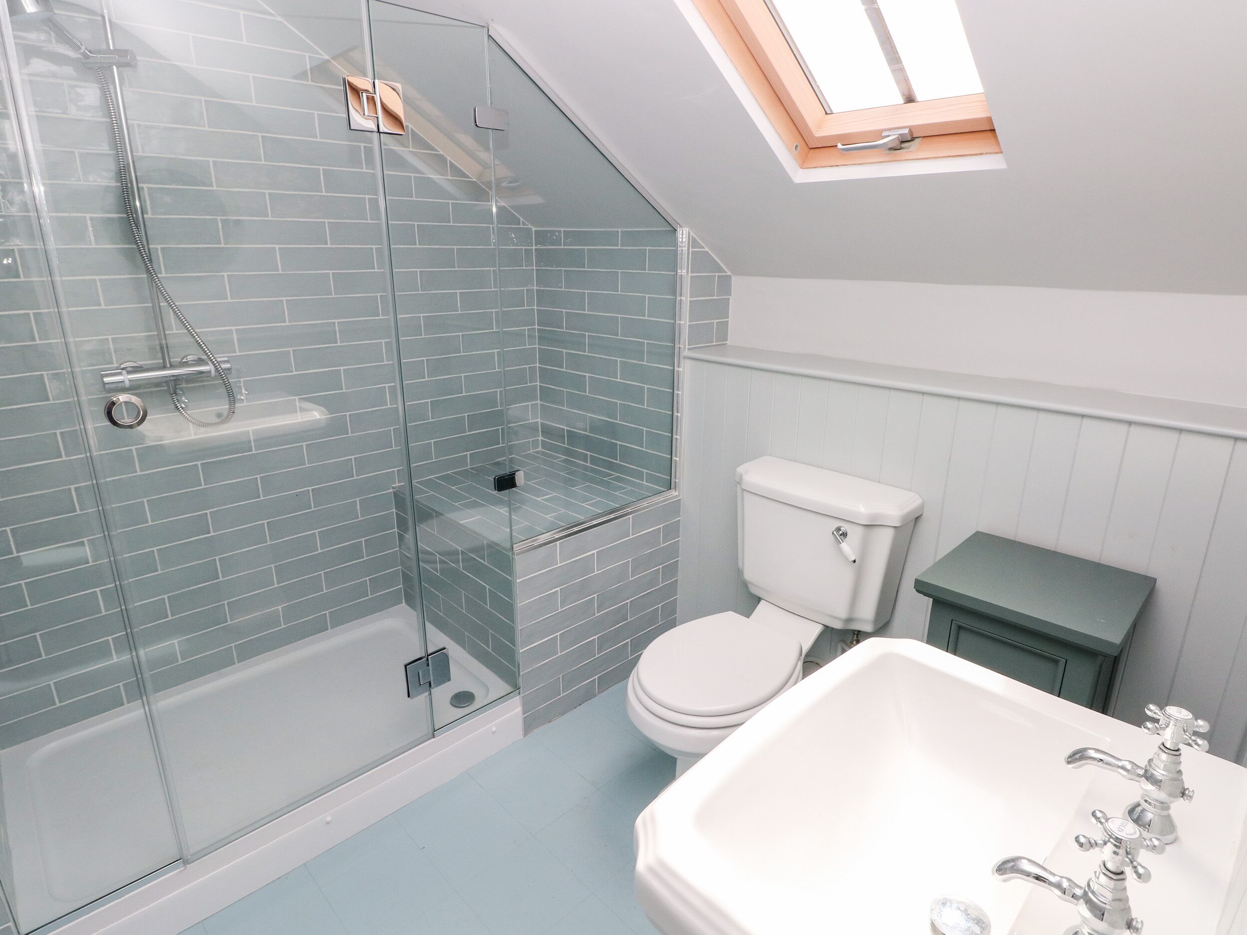 Een badkamer met een douchecabine van glas, een wit toilet en een wastafel met twee kraanwerk.