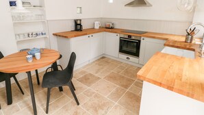 A compact kitchen with white cabinets, a wooden countertop, a built-in oven, and a dining area with a table and chairs. - 10 Westgate Hill (Pembroke)