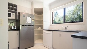 Une cuisine moderne équipée d’un four à micro-ondes encastré, d’un réfrigérateur en acier inoxydable et d’un lave-vaisselle. Une fenêtre laisse entrer la lumière naturelle et offre une vue sur la verdure environnante.