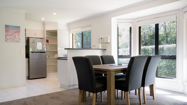 Une cuisine moderne dotée d’un réfrigérateur encastré, d’un coin repas avec une table en bois et quatre chaises, et de grandes fenêtres offrant une vue sur l’extérieur.