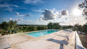A rectangular swimming pool with a stone deck, surrounded by greenery and trees. - Old trullo and lamia in one hectar garden pool with view. (Ostuni)