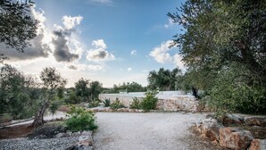 A gravel pathway leading to a stone wall with a view of a garden and trees. - Old trullo and lamia in one hectar garden pool with view. (Ostuni)