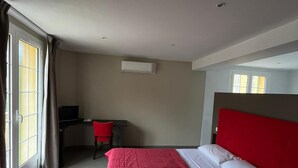 A hotel room with a bed, a desk, a chair, and an air conditioning unit.