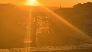 A sunset over a coastal area with buildings silhouetted against the sky.