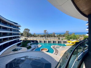 A modern hotel with a pool area, including a central pool and a smaller circular pool, surrounded by lounge areas and a view of the ocean. - 1 bedroom apartment in antalya (Antalya)