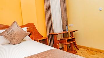 A neatly arranged hotel room with a bed, wooden nightstand, and a small wooden table.