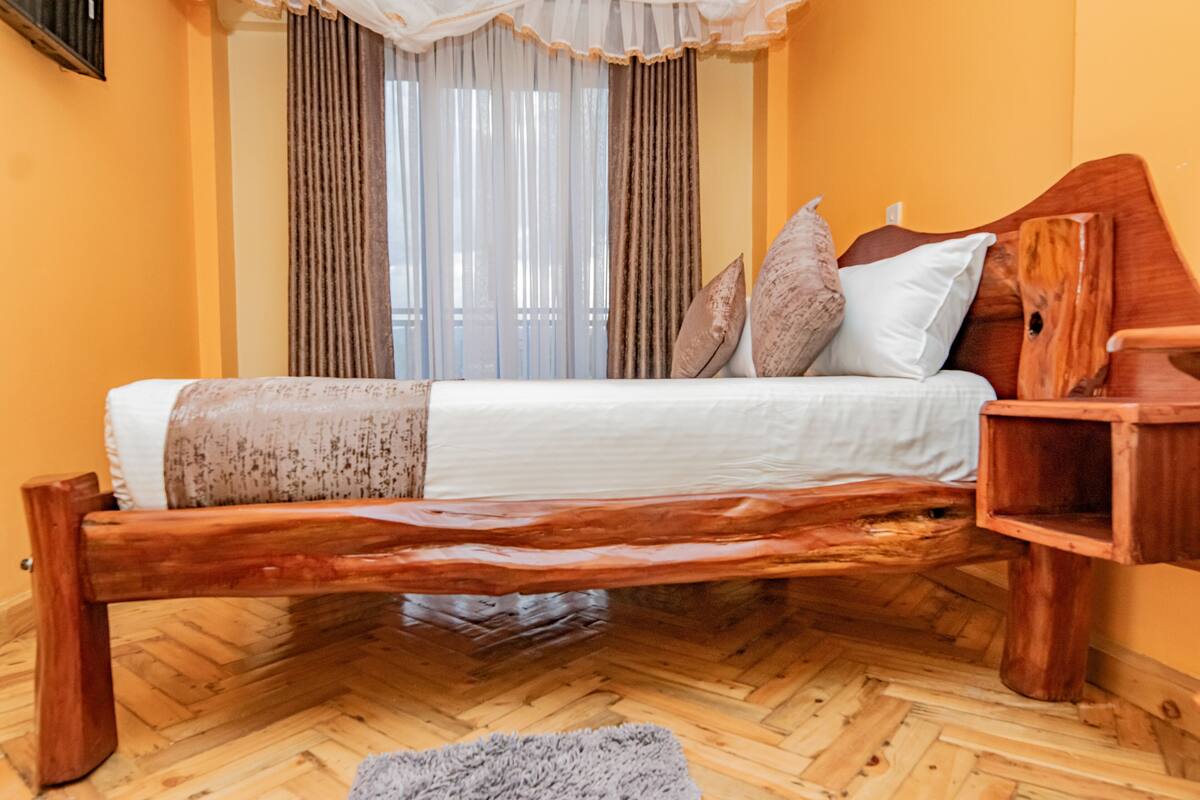 Uma cama de madeira com cabeceira, uma mesa de cabeceira e uma janela com cortinas.