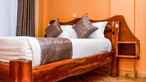 A wooden bed with white and brown bedding, a nightstand, and a wooden headboard. - Ambrosia Hotel (Naivasha)
