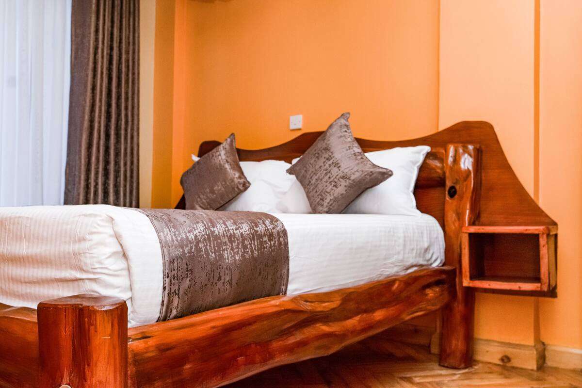 Uma cama de madeira com roupa de cama branca e castanha, uma mesa de cabeceira e uma cabeceira de madeira.