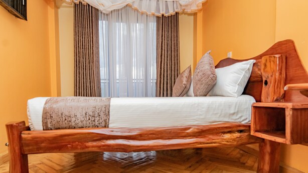 A bed with a wooden frame, a headboard, and a bedside table. - Ambrosia Hotel (Naivasha)