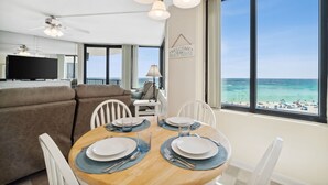 A dining area with a view of the beach, a sofa, and a TV in the background.
