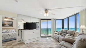 A spacious living room with a large sofa, a television, and a balcony with ocean views.