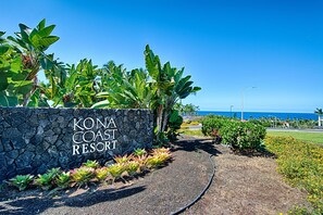 Skilt for Kona Coast Resort med udsigt over havet og tropisk vegetation.