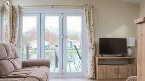 Una sala de estar con un sofá, un televisor sobre un mueble de madera y un ventanal corredizo que da a un área exterior.