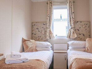 A hotel room with two beds, a window with curtains, a radiator, and a small cabinet.