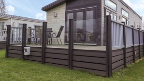 Una casa móvil moderna con un gran ventanal, una terraza y revestimiento oscuro.