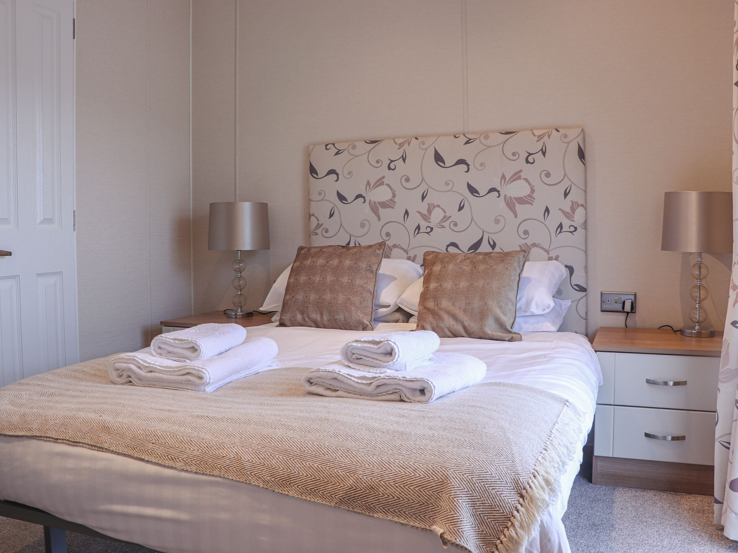 A neatly made bed with folded towels, a patterned headboard, and bedside lamps.