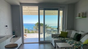 A modern living room with a sofa, a small table, and a view of the ocean through large sliding glass doors. - Beachfront apartment with fantastic terrace facing the Ionian Sea (Ardore Marina)