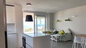 A modern kitchen with a large island, a dining area with white furniture, and a view of the sea through a sliding glass door. - Beachfront apartment with fantastic terrace facing the Ionian Sea (Ardore Marina)