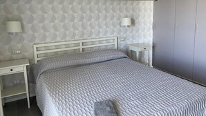 A bedroom with a bed, two bedside tables, a nightstand, a wardrobe, and a geometric-patterned wall. - Beachfront apartment with fantastic terrace facing the Ionian Sea (Ardore Marina)