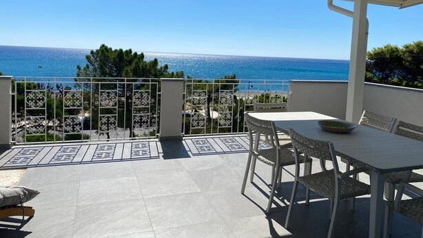 A covered outdoor area with a table and chairs, a view of the sea, and a decorative metal fence. - Beachfront apartment with fantastic terrace facing the Ionian Sea (Ardore Marina)