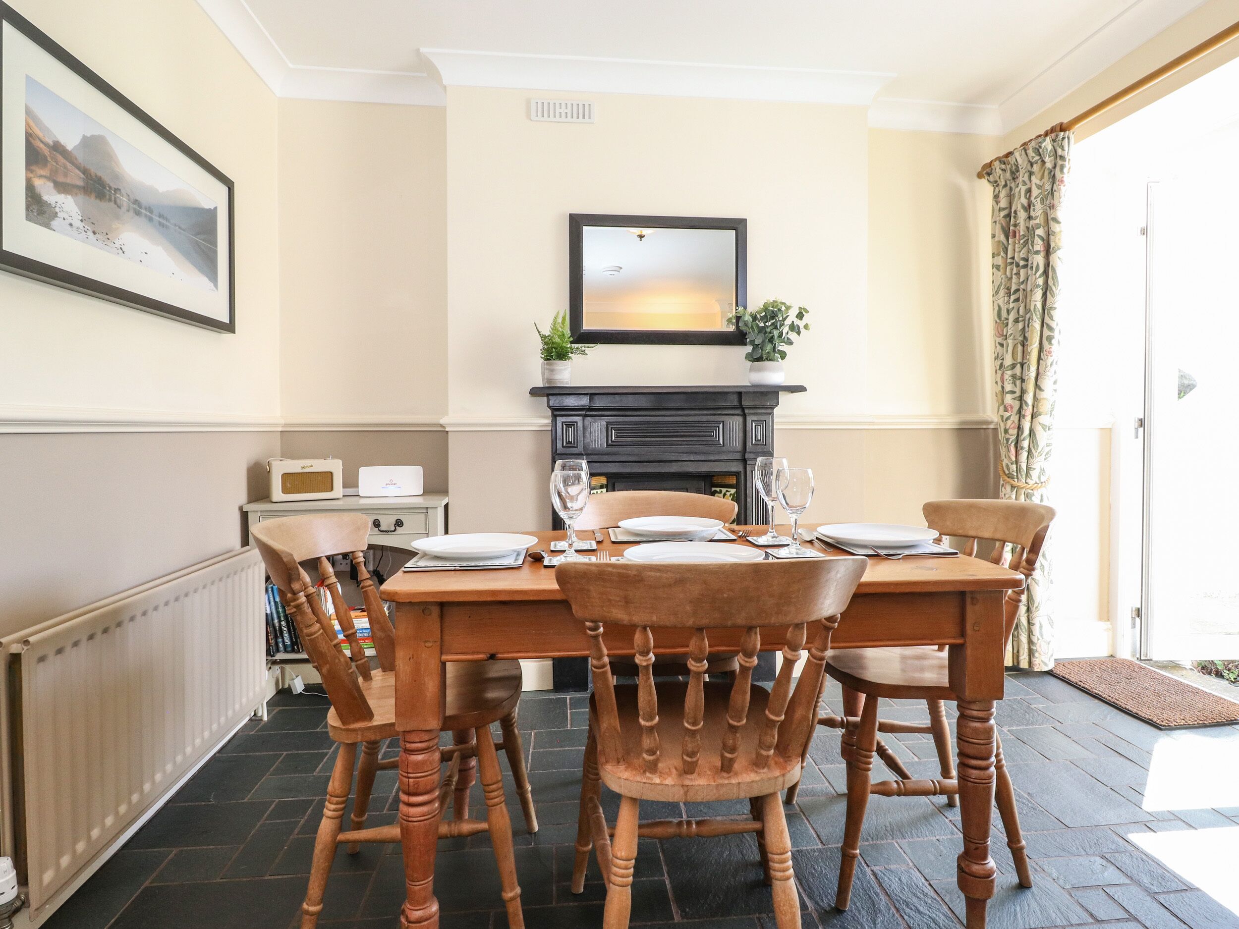 A dining room with a wooden table set for four, flanked by two chairs, a fireplace, and a framed picture on the wall.
