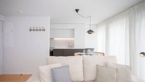 Ein modernes Wohnzimmer mit einer Couch, einem Esstisch mit Stühlen, einer Küchenzeile und einem Garderobenständer.
