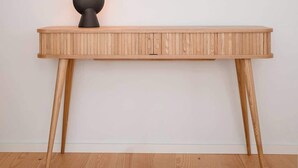 Ein Holzkonsolentisch mit einem runden Spiegel darüber, einer Wandleuchte und einer Tischlampe.