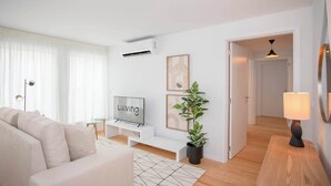 Ein modernes Wohnzimmer mit einer Couch, einem Fernseher, einer Topfpflanze und einer Lampe.