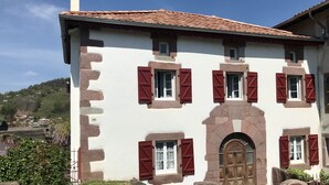 Un edificio tradizionale con tetto in tegole, persiane rosse e un ingresso in pietra.