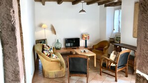 Un accogliente soggiorno con soffitto in legno, televisione, lampada e una poltrona con cuscino colorato.