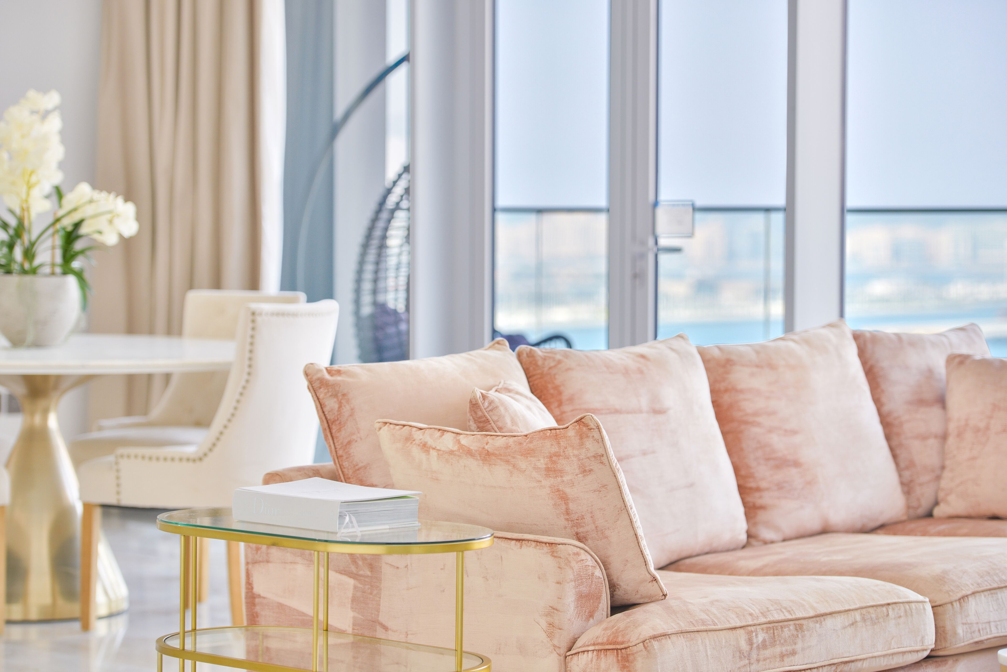 A modern living room with a beige sofa, a glass coffee table, and a view of the city through large windows.
