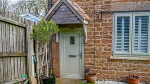 A stone house with a wooden door, a small garden with potted plants, and a window with shutters. - Amazing Guest Cottage in Nottingham with Parking! - Pass the Keys (Nottingham)