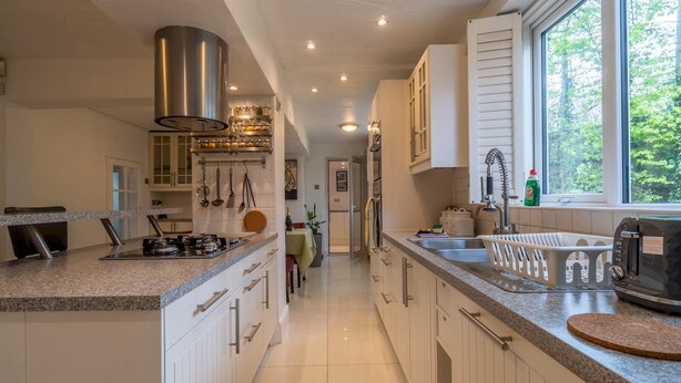 A modern kitchen with white cabinetry, granite countertops, and a large window providing a view of the outdoors. - Amazing Guest Cottage in Nottingham with Parking! - Pass the Keys (Nottingham)