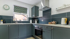 Une cuisine moderne avec des meubles de couleur sombre, un four encastré et une fenêtre agrémentée de rideaux à motifs.