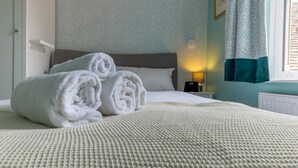 Un lit bien fait, avec des serviettes blanches pliées en rouleau, une lampe de chevet et une fenêtre avec des rideaux.