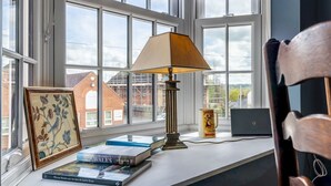Une pièce avec une grande fenêtre, un bureau avec des livres, une lampe et un ordinateur portable.