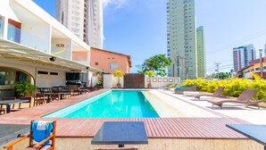 A rooftop pool with lounge chairs and tables, surrounded by high-rise buildings.