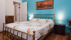 Un dormitorio con cama, mesitas de noche, un cuadro en la pared y una puerta.
