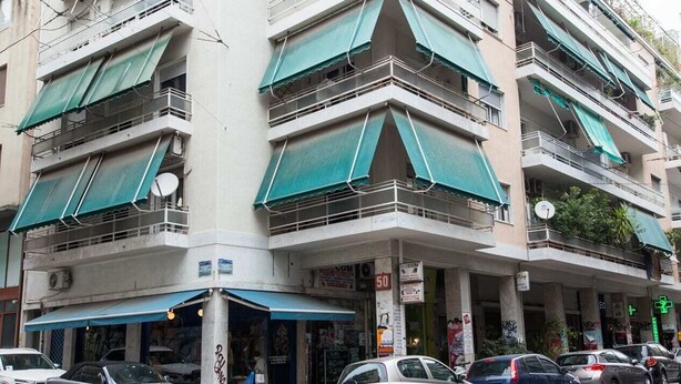 Un edificio de varios pisos con balcones, una tienda en la planta baja y coches aparcados.