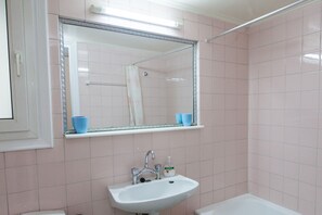 A bathroom with pink tiles, a white sink, a mirror, and a shower area. - Beautiful Retro Apt in Koukaki (Athens)