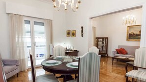 Un comedor con una mesa redonda, sillas y una araña. Se observa un sofá y un aparador al fondo.