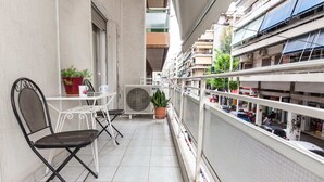 Un balcón con una mesa y sillas blancas, una planta en maceta y un equipo de aire acondicionado.