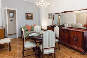 A dining area with a round table, chairs, a sofa, and a wooden cabinet with a mirror. - Beautiful Retro Apt in Koukaki (Athens)