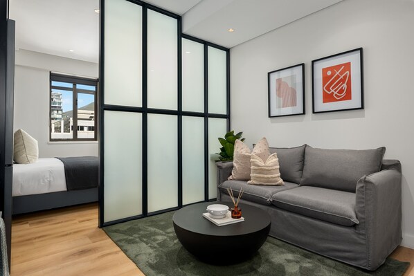 A modern living room with a grey sofa, a black coffee table, and a sliding glass door leading to another room.